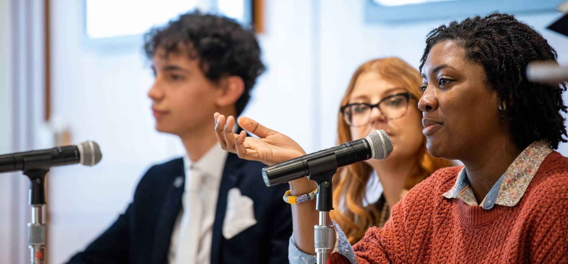 Three students sitting at a panel table answering questions; female student in foreground
